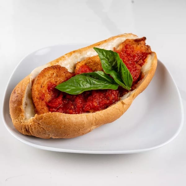 Chicken parmesan hero sandwich with melted cheese, marinara sauce, and fresh basil on a white plate.
