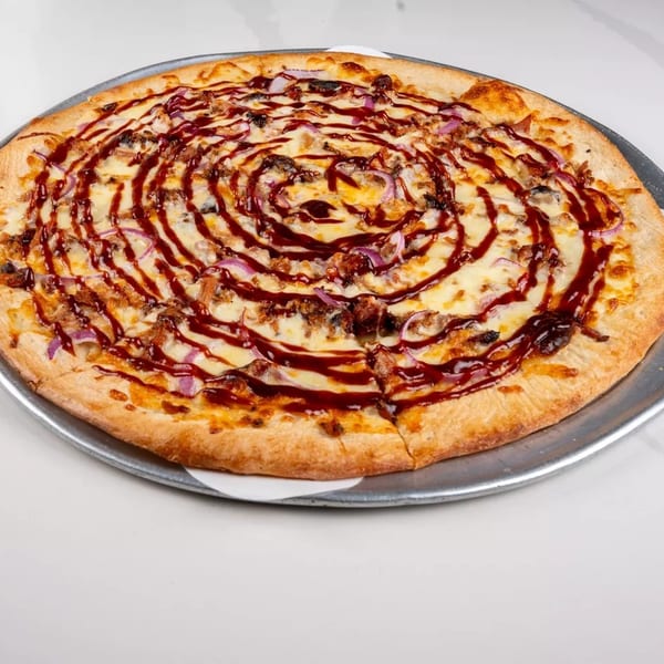 A BBQ chicken pizza with red onions and a swirl of barbecue sauce on a metal tray.