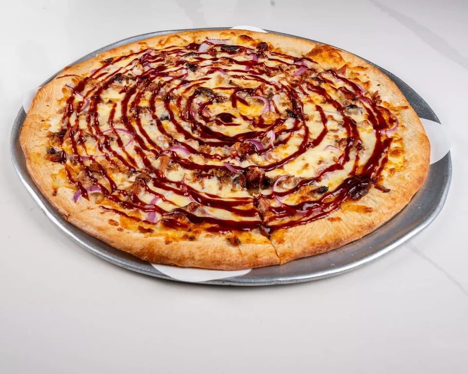 A BBQ chicken pizza with red onions and a swirl of barbecue sauce on a metal tray.