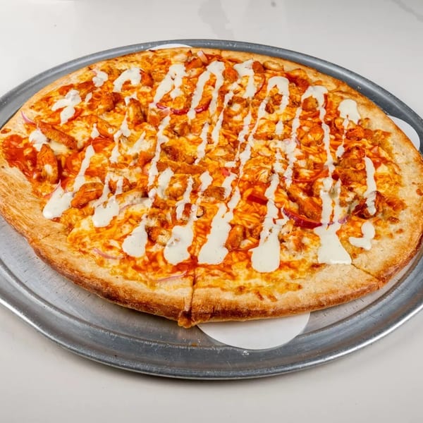 Buffalo chicken pizza with ranch drizzle on a metal tray, ready to be served.