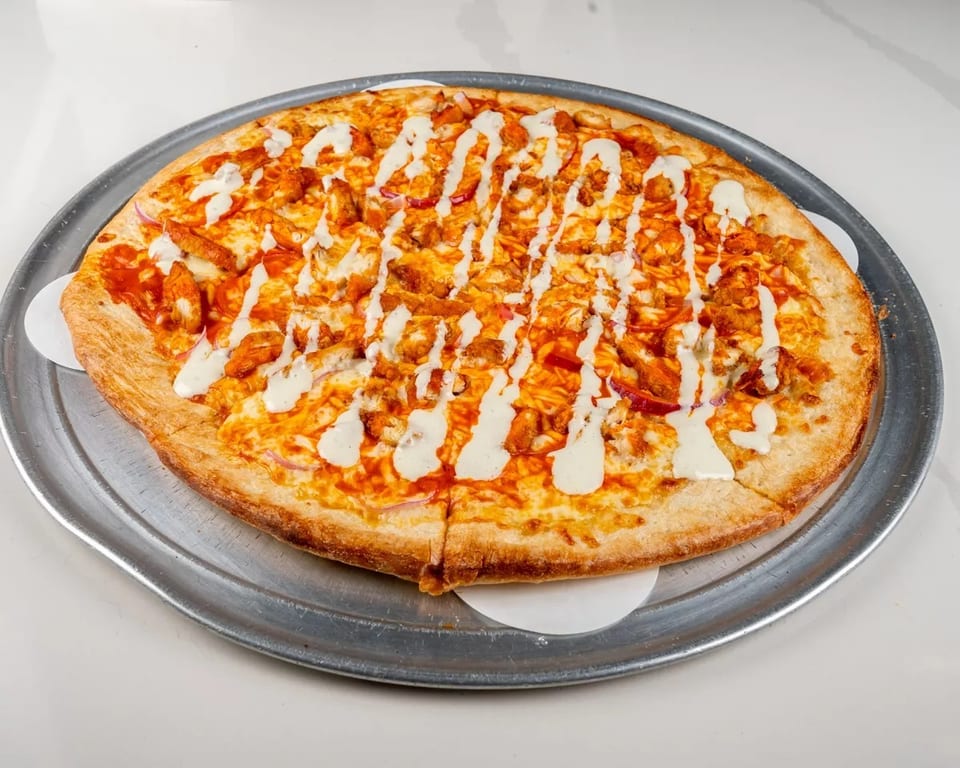 Buffalo chicken pizza with ranch drizzle on a metal tray, ready to be served.