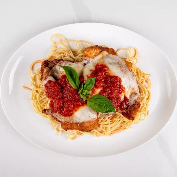 Chicken parmesan with spaghetti, marinara sauce, melted cheese, and fresh basil on a white plate.