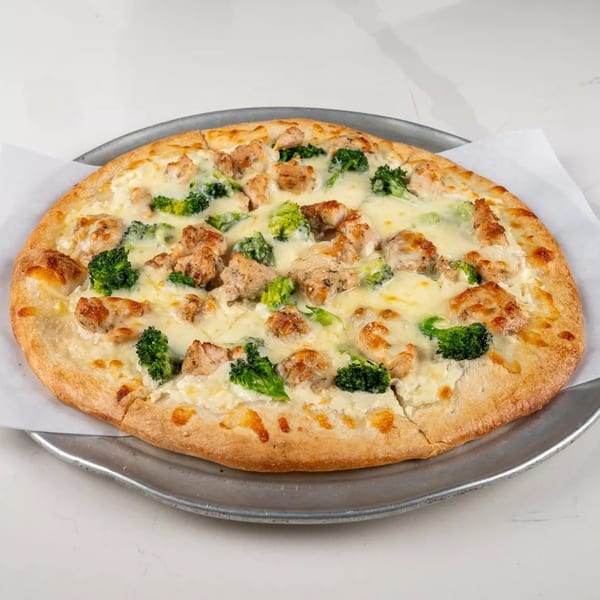 Chicken and broccoli pizza with white sauce on a metal tray, on a white marble surface.
